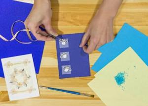 overhead view of two hands making a greeting card from various craft supplies
